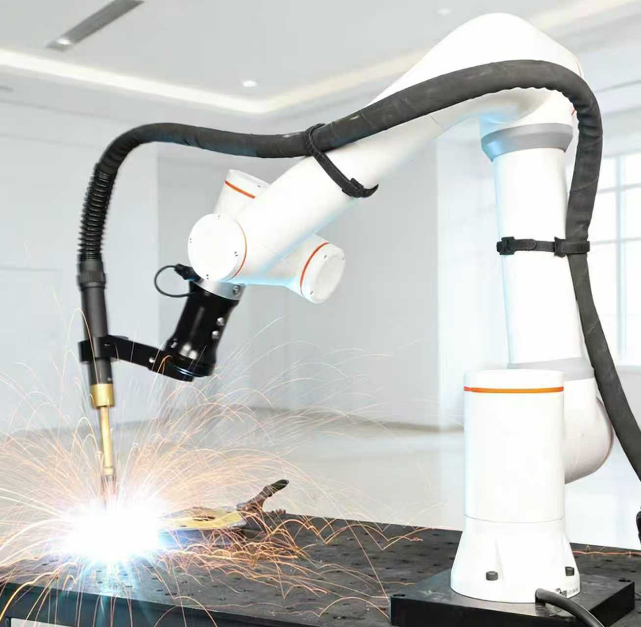 White six-axis collaborative welding cobot laying a MIG bead on a steel part with sparks on a fixture table